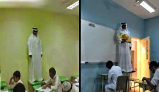 معلم يراقب الإختبارات بنظارة سوداء ويعتلي إحدى الطاولات في قاعة الإختبار